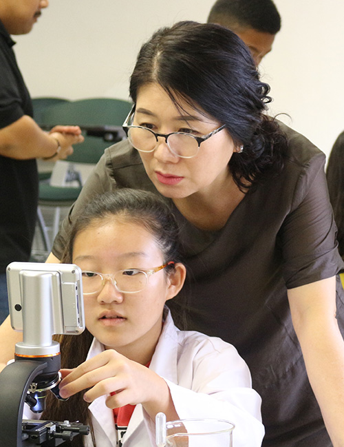 Claire Yi demonstrates to her mother how to prepare a microscope slide and how to operate a microscope.