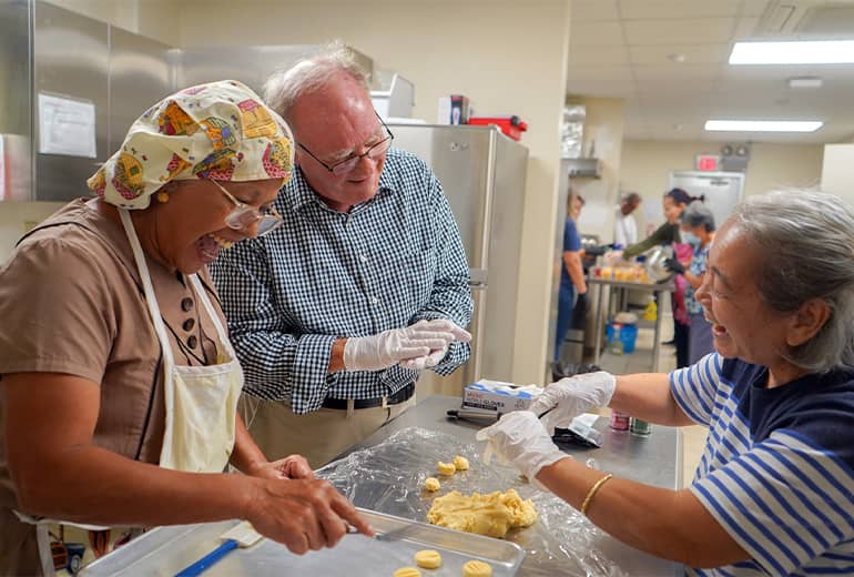 Three "Let's Cook" workshop participants shape dough while laughing and smiling in a kitchen