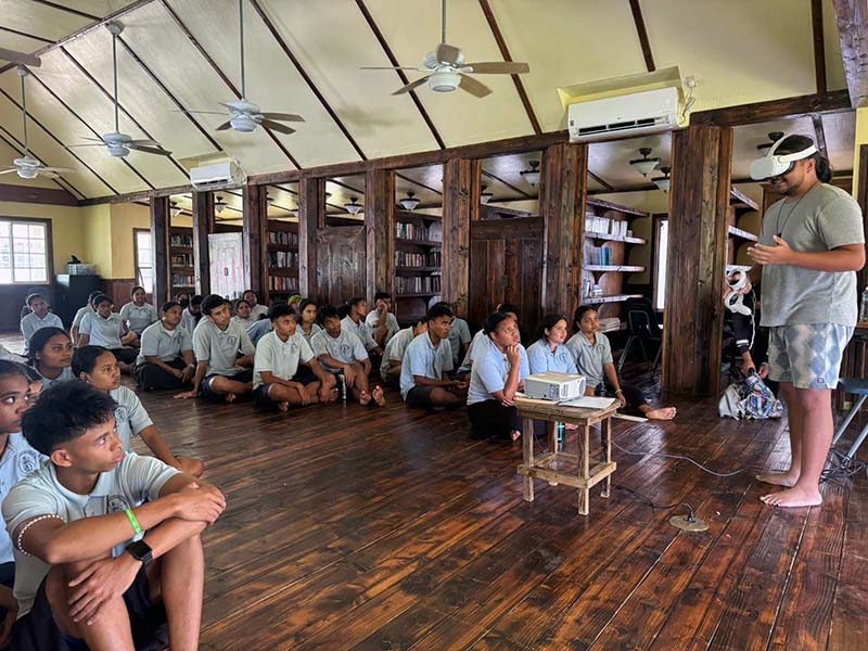 Photo of a person demonstrating a virtual reality headset in front of a classroom 