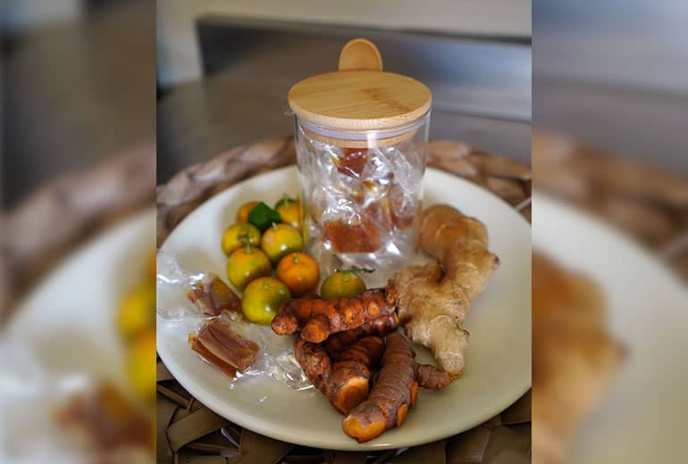 Turmeric candies sit in a jar on a plate next to ginger and calamansi