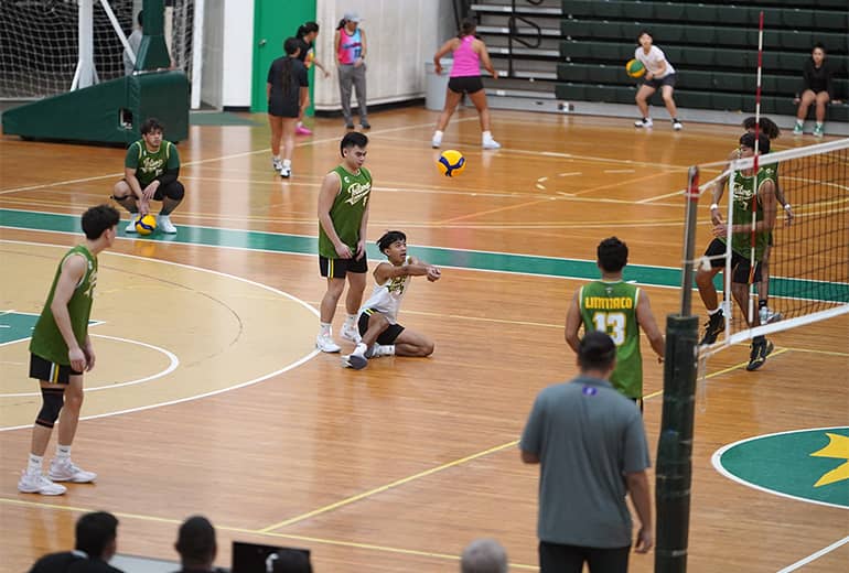 Action shot of UOG men’s volleyball player about to bump the ball surrounded by other players