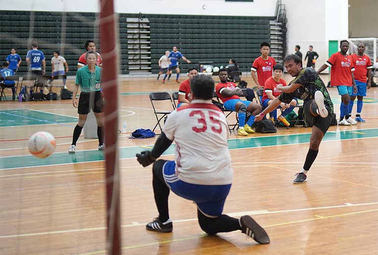 action shot that includes volleyball, coach, the net in a plane close to the camera, and the volleyball players