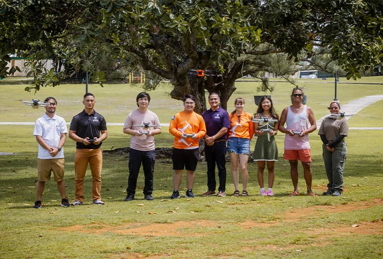 Fourth cohort of UOG Drone Corps flies drones outdoors while posing for photo