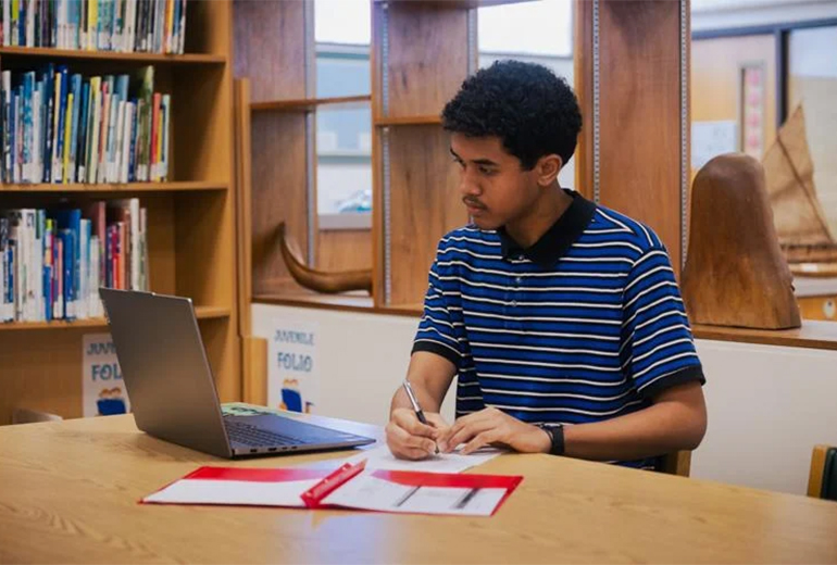 Young man sits at desk with laptop grading assignments