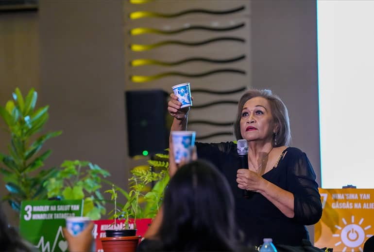 Mama Lou, with a microphone in hand, holds cups in the air with audience members of G3 workshop.